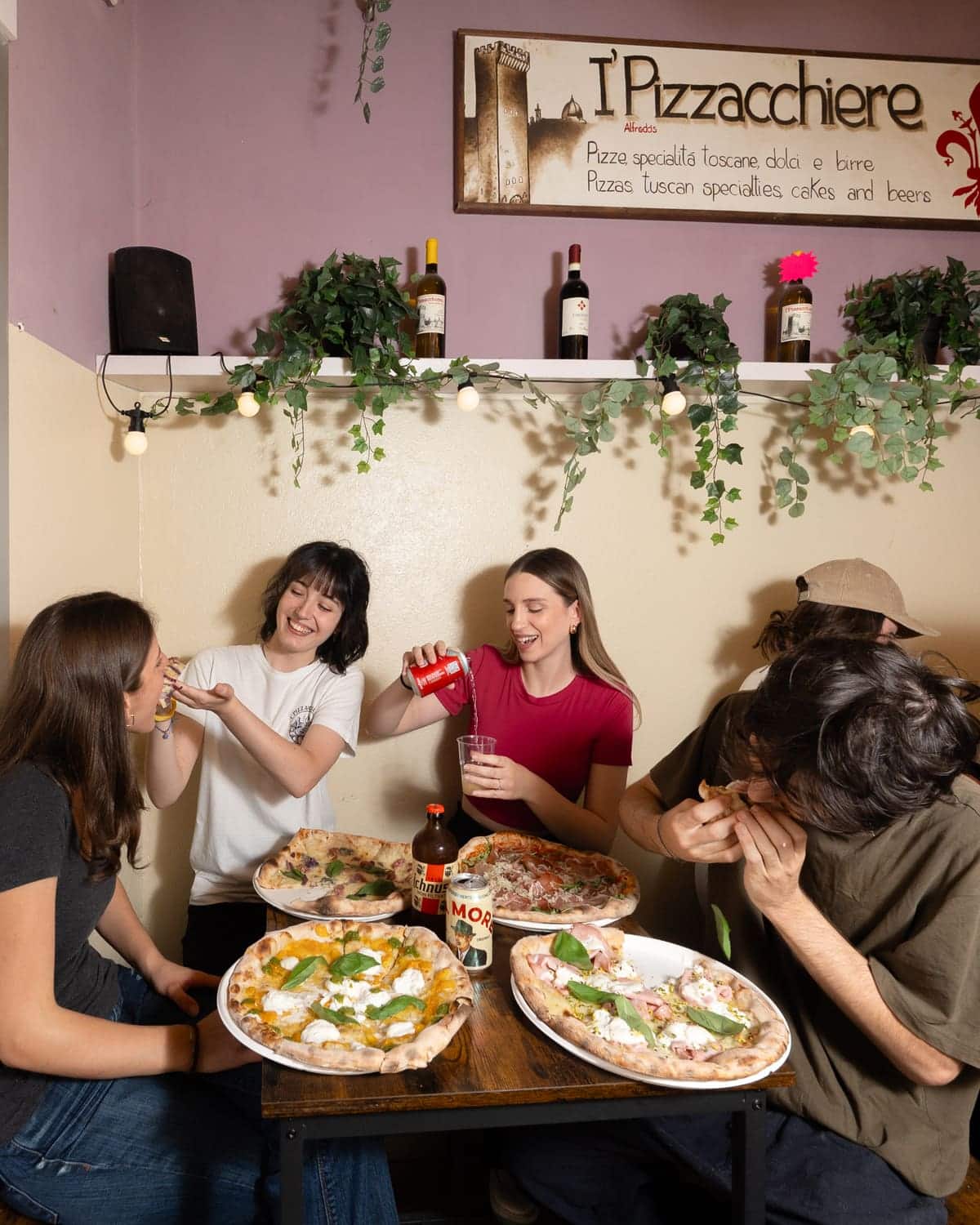 Quattro persone a tavola, tre pizze in mezzo e i bicchieri alzati.